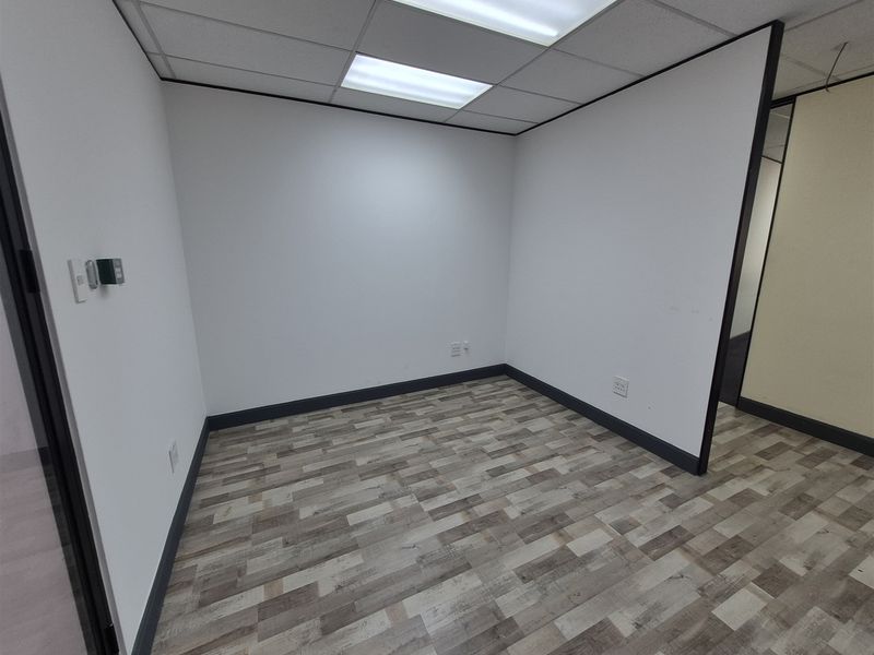 A clean, empty office space featuring modern vinyl plank flooring, a suspended ceiling with recessed lighting, and neutral partition walls.