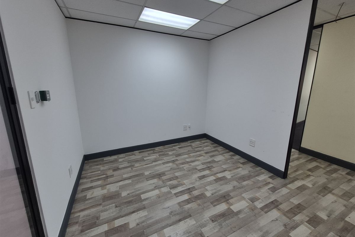 A clean, empty office space featuring modern vinyl plank flooring, a suspended ceiling with recessed lighting, and neutral partition walls.