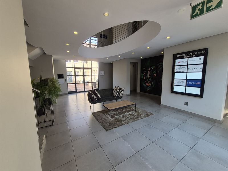 Modern office park entrance lobby featuring a central atrium void, tiled flooring, and a directory board for building tenants.