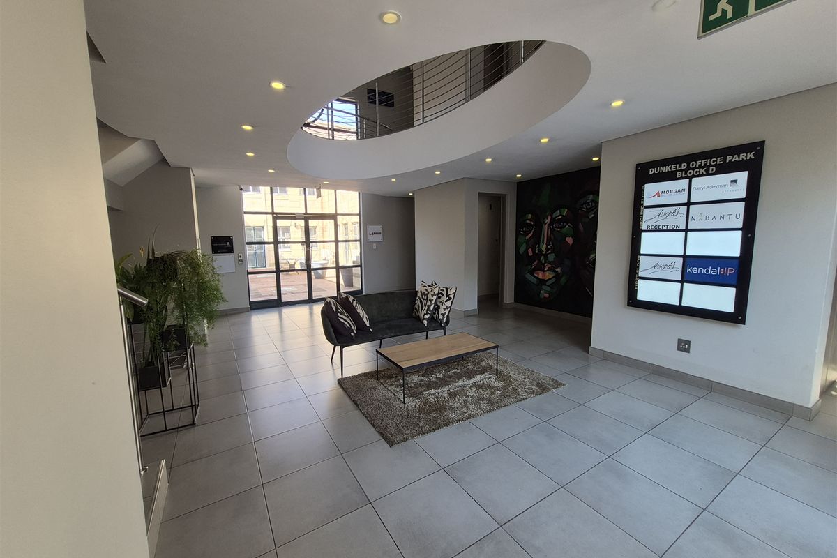 Modern office park entrance lobby featuring a central atrium void, tiled flooring, and a directory board for building tenants.