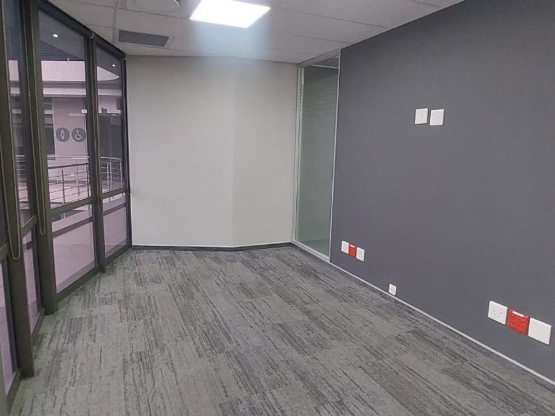 A vacant, modern office space featuring grey carpeted flooring, a glass partition wall, and integrated electrical and data connectivity points.
