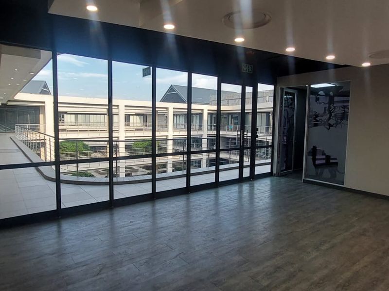 Modern, empty office space featuring floor-to-ceiling windows with views of the commercial courtyard, recessed lighting, and high-quality laminate flooring.