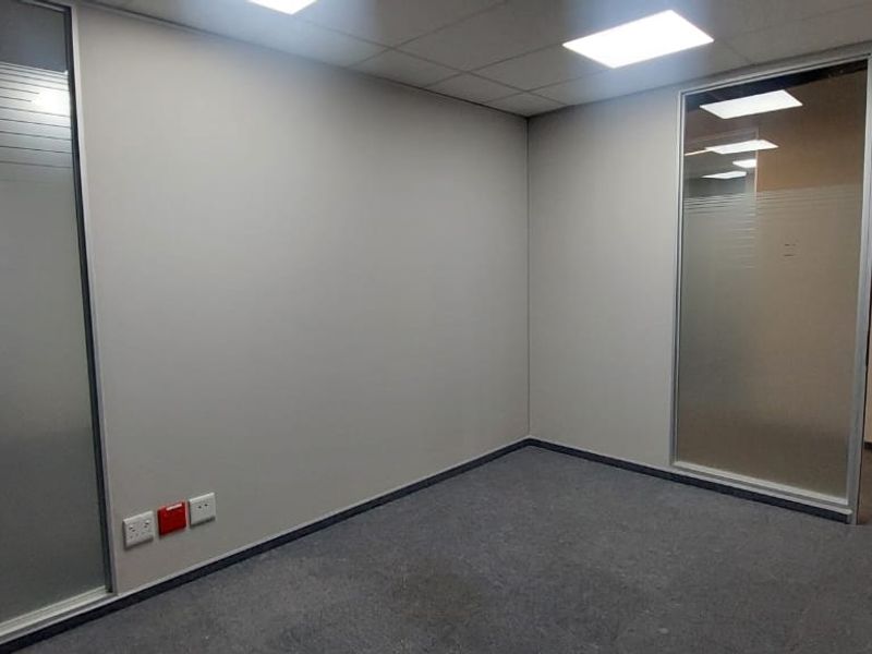 A clean, empty office space featuring modern glass partitions, neutral carpet flooring, and recessed ceiling lighting, suitable for a professional workspace.