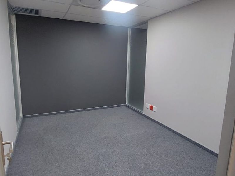 A clean, vacant office space featuring modern glass partitions, carpeted flooring, and a suspended ceiling with integrated lighting.