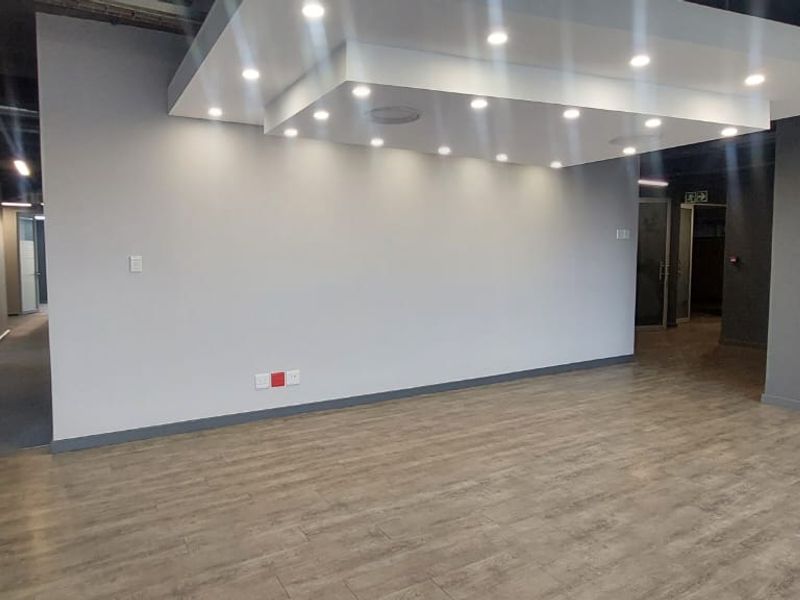 Modern open-plan office space featuring wood-look tile flooring, a contemporary drop ceiling with recessed lighting, and glass partition walls.