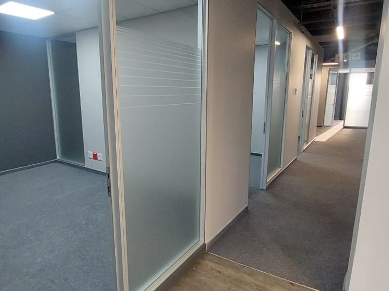 Modern commercial office space featuring glass partition walls, carpeted flooring, and recessed lighting, providing a clean and professional environment.