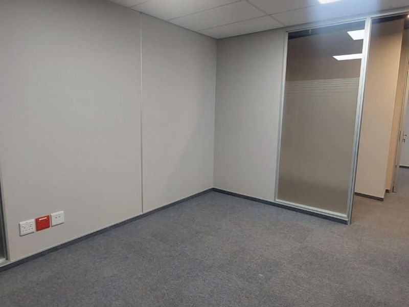 A clean, empty commercial office space featuring frosted glass partitions, carpeted flooring, and a suspended ceiling, suitable for a professional workspace.