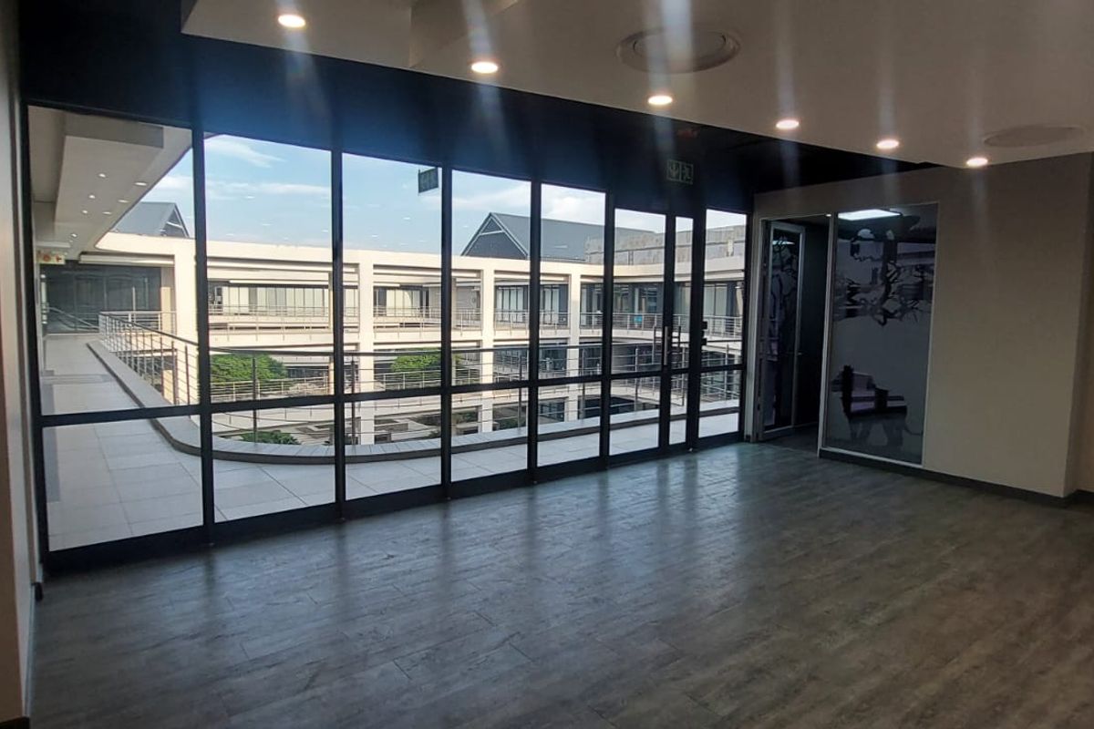 Modern, empty office space featuring floor-to-ceiling windows with views of the commercial courtyard, recessed lighting, and high-quality laminate flooring.