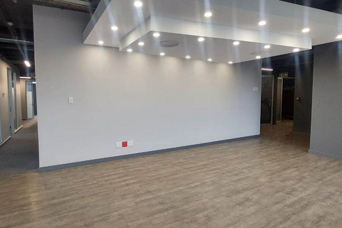 Modern open-plan office space featuring wood-look tile flooring, a contemporary drop ceiling with recessed lighting, and glass partition walls.