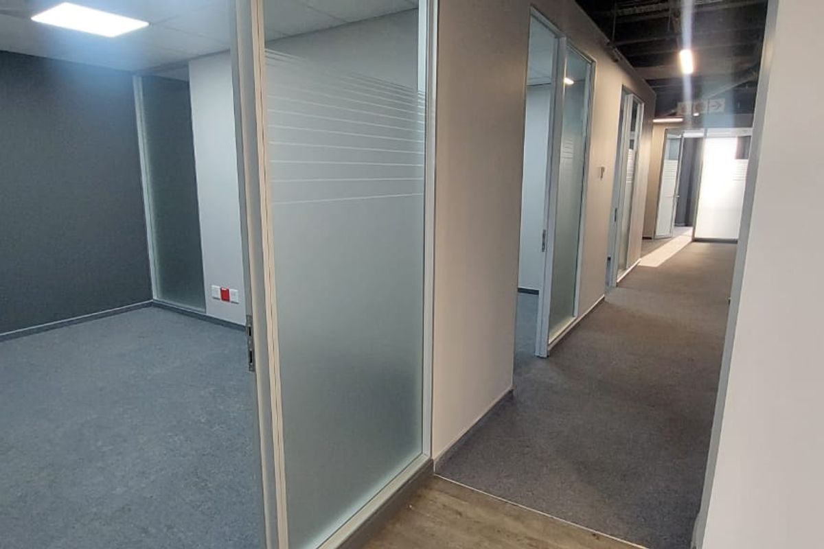 Modern commercial office space featuring glass partition walls, carpeted flooring, and recessed lighting, providing a clean and professional environment.