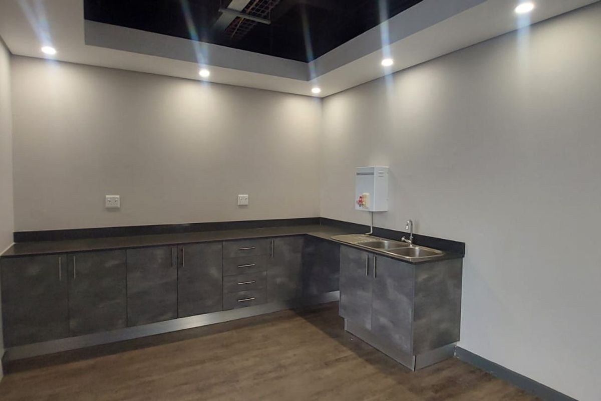 A modern, clean commercial kitchenette featuring dark grey cabinetry, a stainless steel double sink, and recessed ceiling lighting.