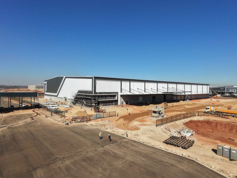 Aerial view of a large industrial warehouse facility under construction, featuring a security gatehouse, perimeter fencing, and extensive site development.