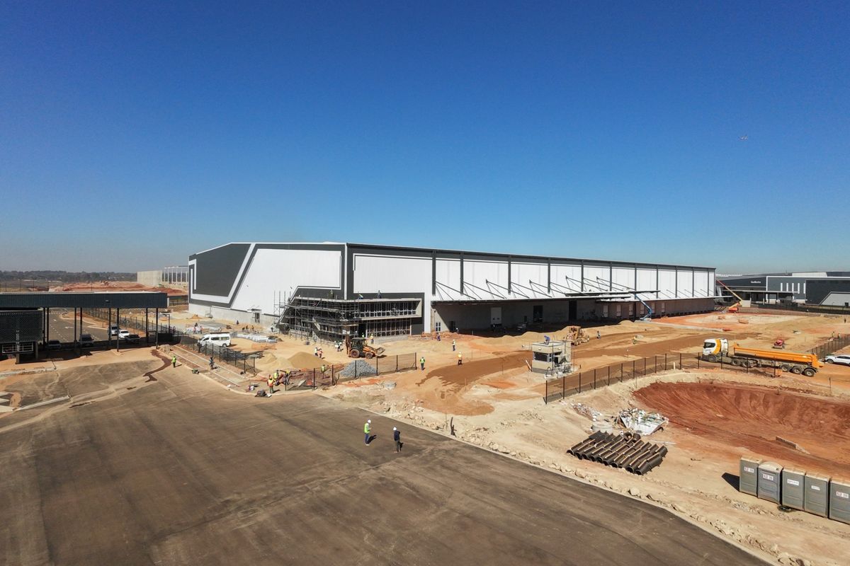Aerial view of a large industrial warehouse facility under construction, featuring a security gatehouse, perimeter fencing, and extensive site development.