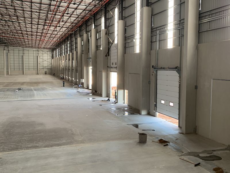 Spacious industrial warehouse featuring high ceilings, exposed steel structural columns, concrete flooring, and multiple roller shutter doors for efficient loading access.