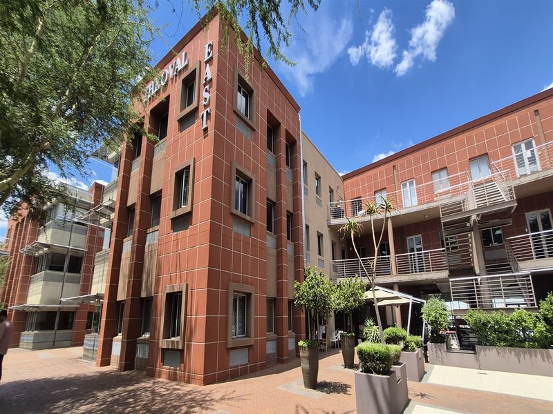 Exterior view of a multi-story office building featuring a red brick facade, metal staircases, and a paved courtyard entrance area.
