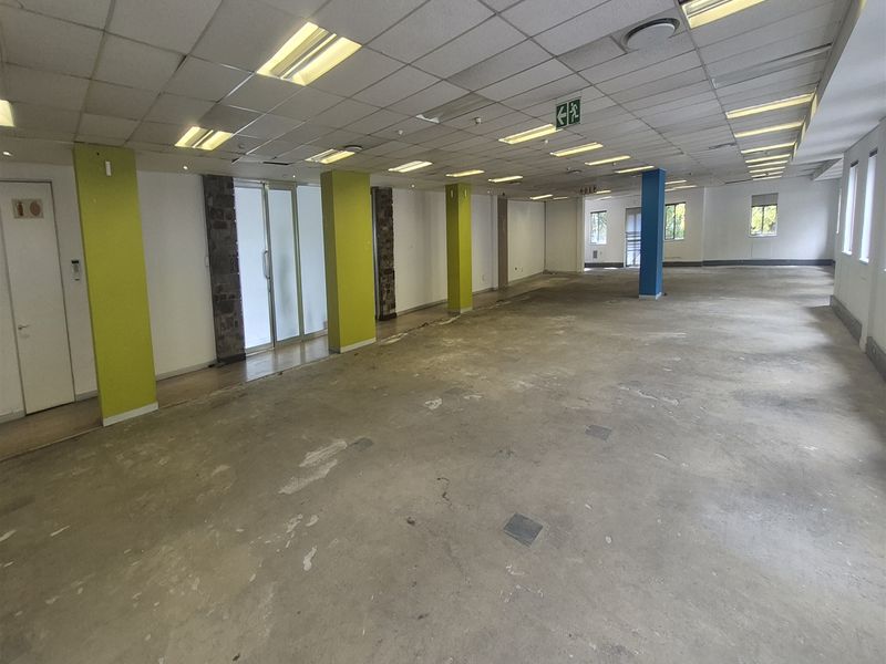 A large, open-plan office space featuring a suspended ceiling, recessed lighting, and structural columns, currently in a shell condition awaiting flooring and interior finishes.