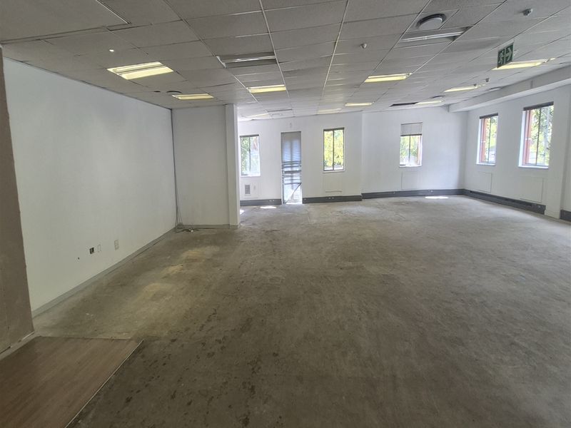 A spacious, vacant open-plan office area featuring a suspended ceiling, recessed lighting, and exposed concrete flooring, ready for custom fit-out.
