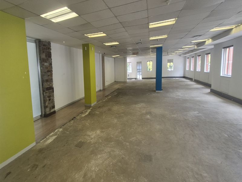 Spacious open-plan office area featuring a suspended ceiling, recessed lighting, and large windows, currently requiring new flooring and cosmetic updates.