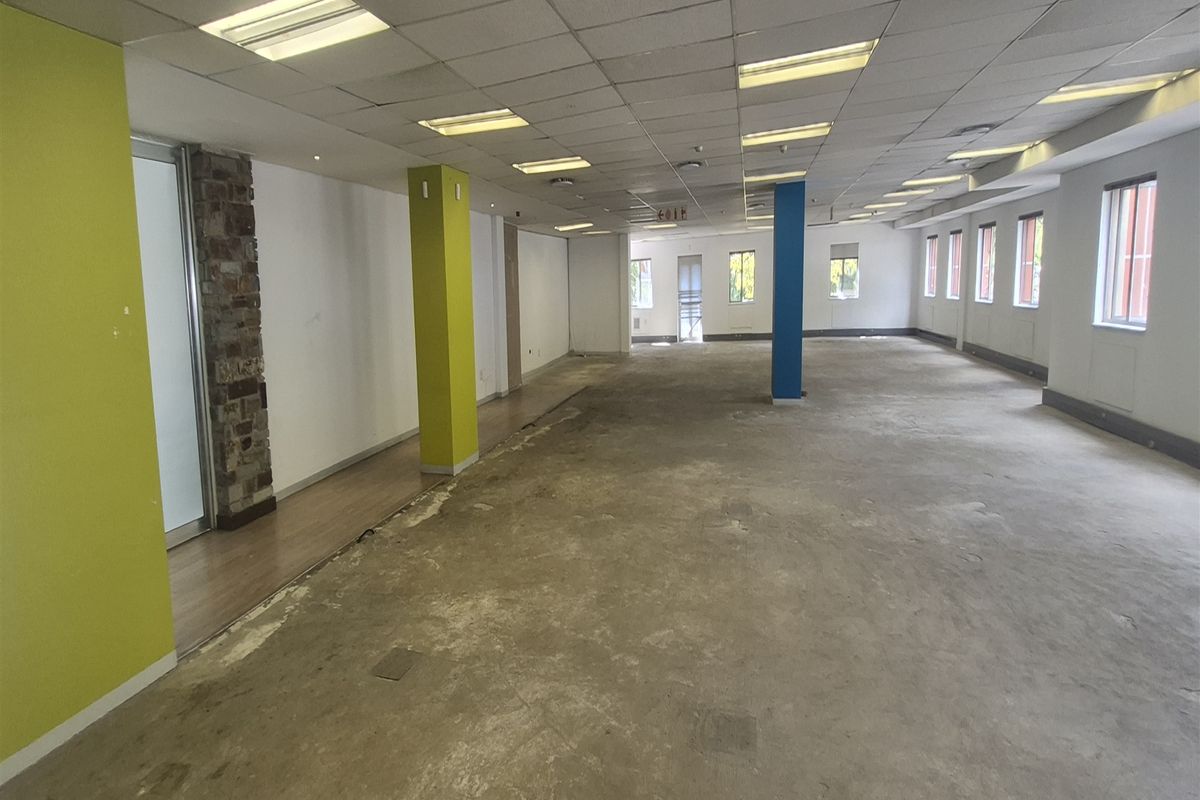 Spacious open-plan office area featuring a suspended ceiling, recessed lighting, and large windows, currently requiring new flooring and cosmetic updates.