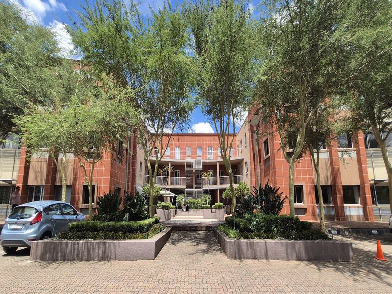 A well-maintained office building complex featuring a red brick facade, central courtyard access, and landscaped garden beds with paved driveway.