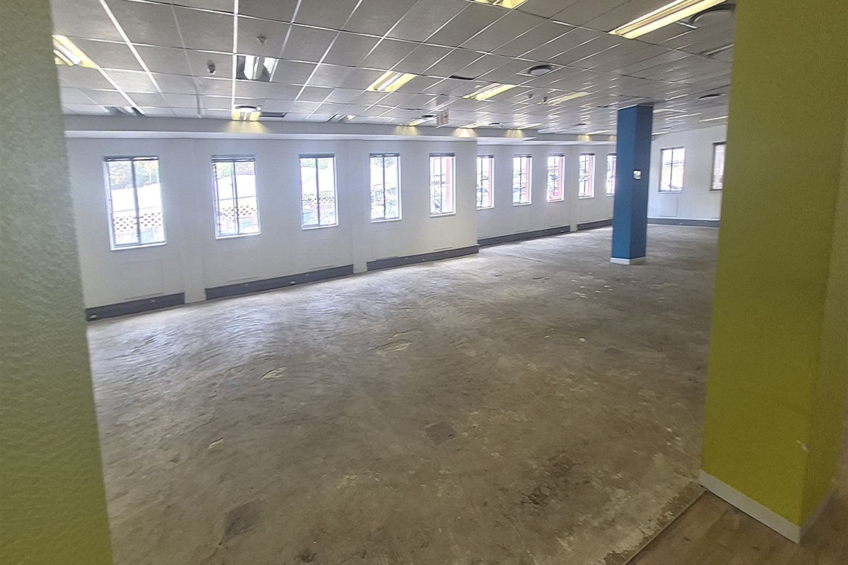 A large, open-plan office space featuring a suspended ceiling, fluorescent lighting, and multiple windows, currently awaiting flooring installation.