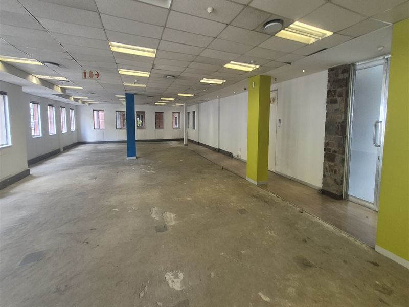 An expansive, empty open-plan office space featuring a suspended ceiling, recessed lighting, and a stone-clad pillar, ready for custom fit-out.