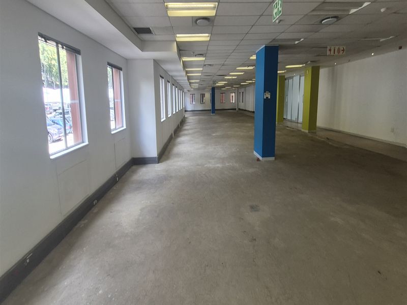 A large, open-plan office space featuring a suspended ceiling, recessed lighting, and multiple windows, currently in a shell condition awaiting flooring and fit-out.