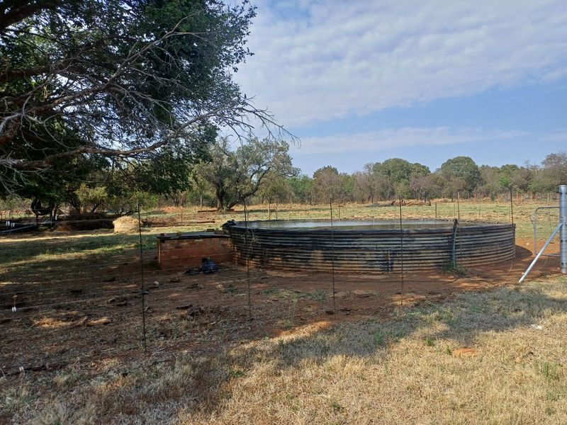 Outdoor farm area featuring a large corrugated steel water reservoir and wire fencing set within a natural landscape.