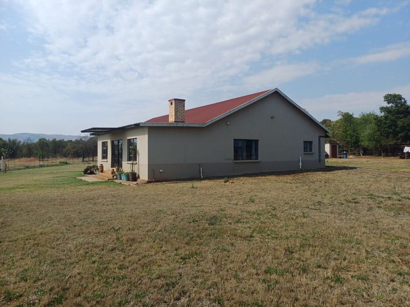 Rear view of a single-story farm house featuring a red metal roof, brick chimney, and a small timber deck area.