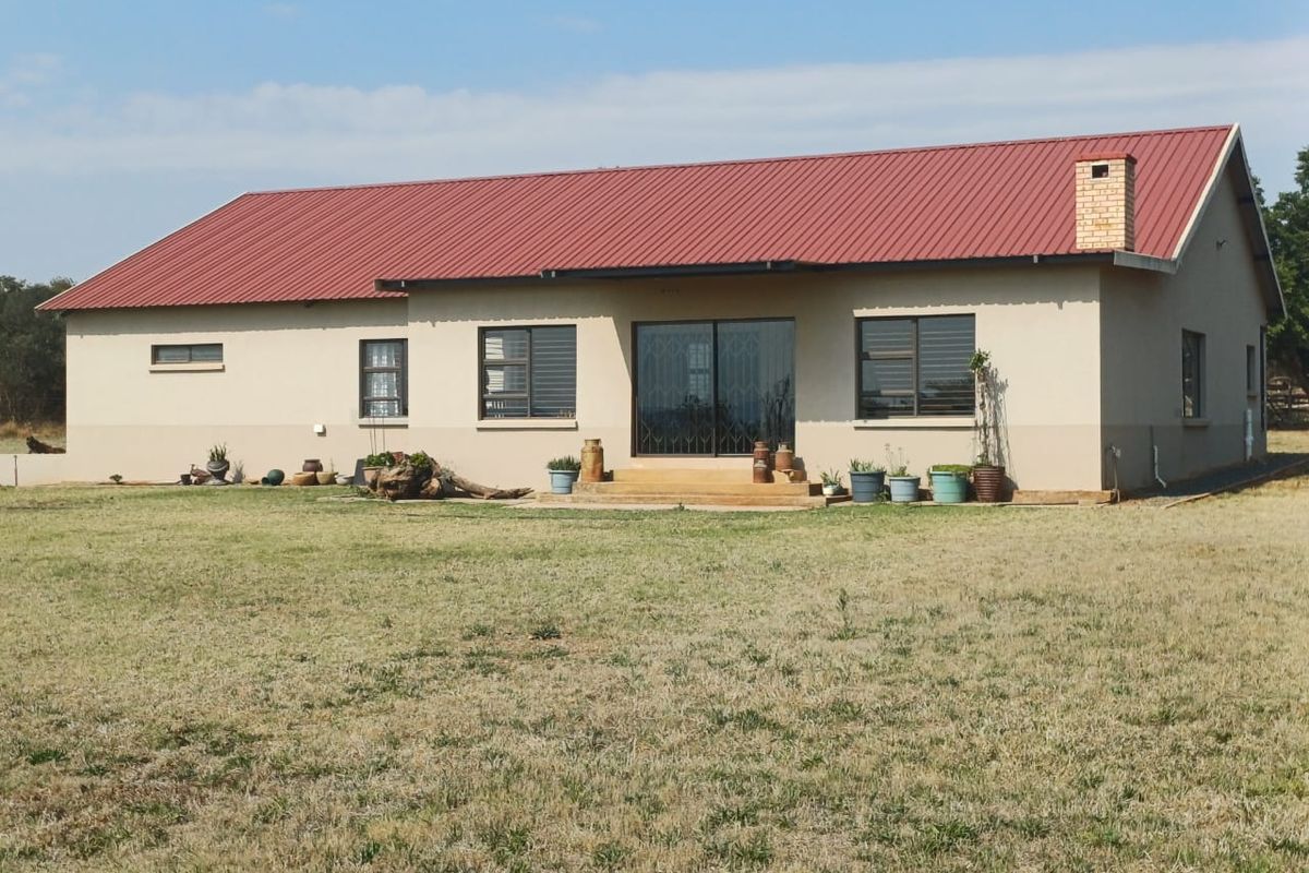 Rear view of a single-story farm house featuring a red corrugated metal roof, brick chimney, and sliding glass door access to the garden.