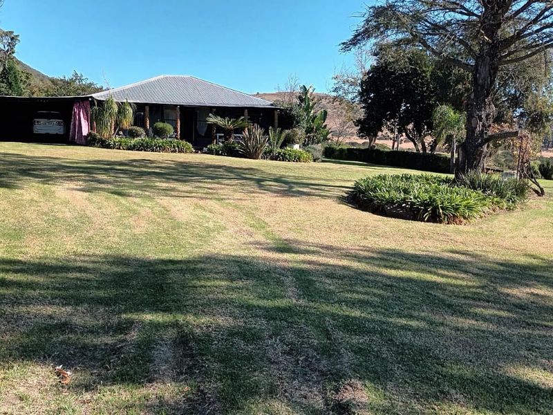 A wide-angle view of the rear exterior of the farmhouse, featuring a covered patio area, expansive lawn, and established garden surroundings.