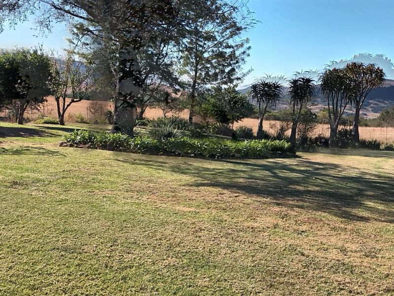 Expansive farm garden featuring mature trees, landscaped garden beds, and open lawn areas with scenic mountain views in the background.