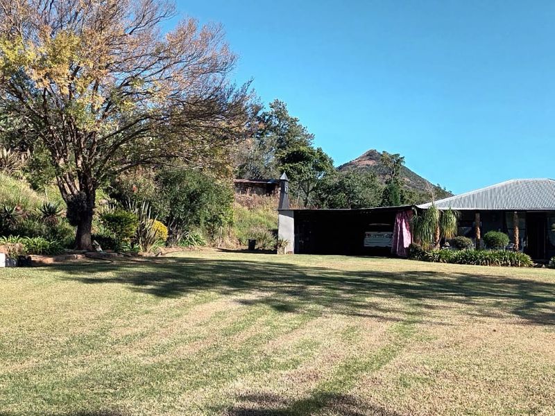 A spacious rear garden area featuring a well-maintained lawn, mature trees, and a covered patio attached to the main farmhouse structure.