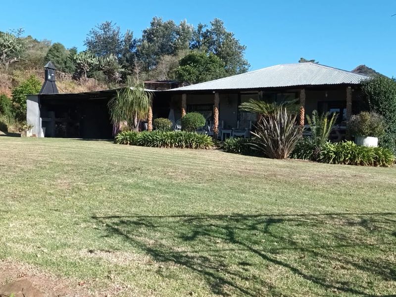 A rear view of the farmhouse featuring a covered patio area with an outdoor fireplace, set within a spacious, well-maintained garden landscape.