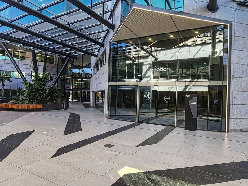 Modern office building entrance featuring a glass atrium, stone paved courtyard, and a prominent reception area with contemporary architectural design.