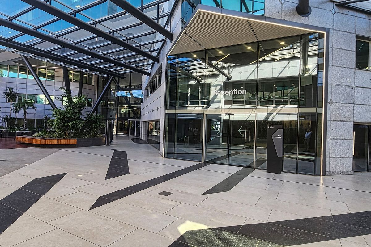 Modern office building entrance featuring a glass atrium, stone paved courtyard, and a prominent reception area with contemporary architectural design.