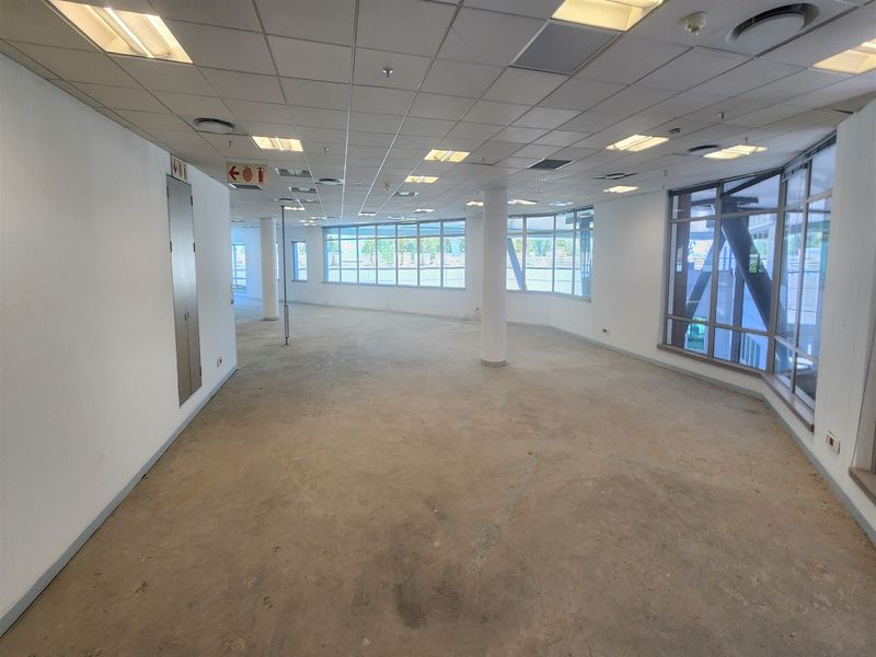 A spacious, vacant open-plan office area featuring large windows, suspended ceilings with recessed lighting, and structural columns, ready for custom flooring and fit-out.