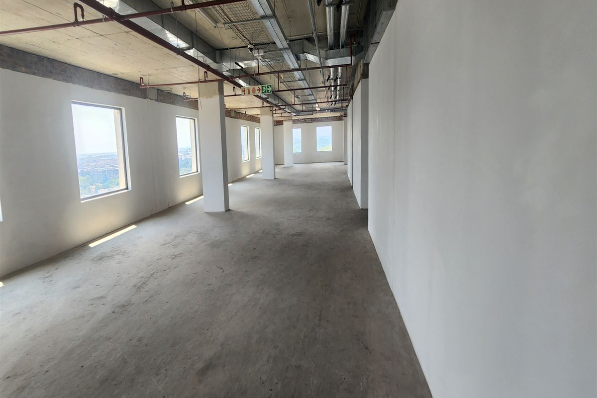 An expansive, open-plan office space in shell condition, featuring exposed industrial ceilings, concrete floors, and large windows providing ample natural light.