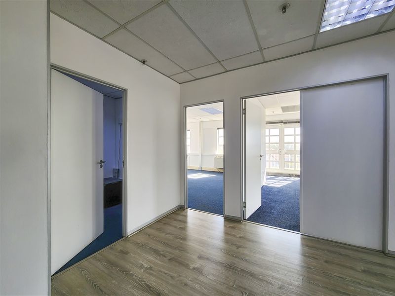 An empty office space featuring a mix of laminate and carpet flooring, suspended ceilings, and multiple internal doorways leading to adjacent office areas.