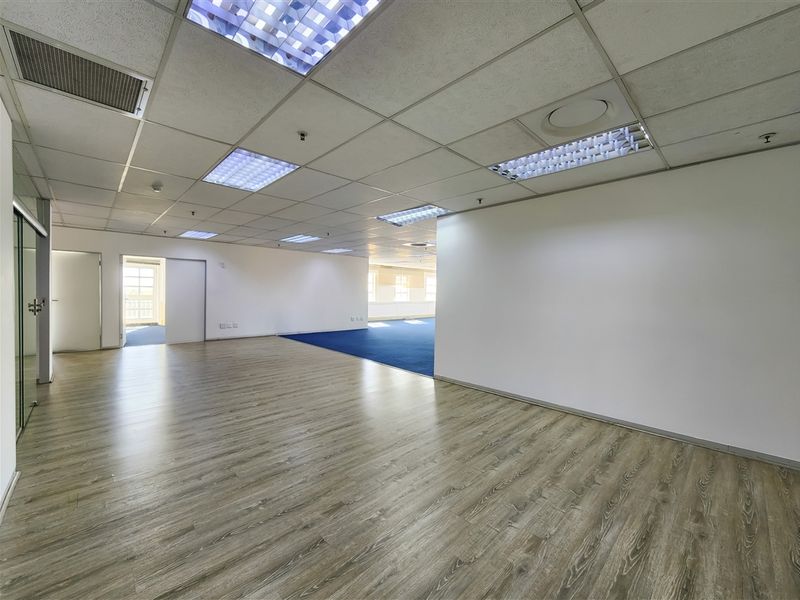 Spacious open-plan office area featuring modern laminate flooring, suspended ceilings with recessed lighting, and glass partitioning.