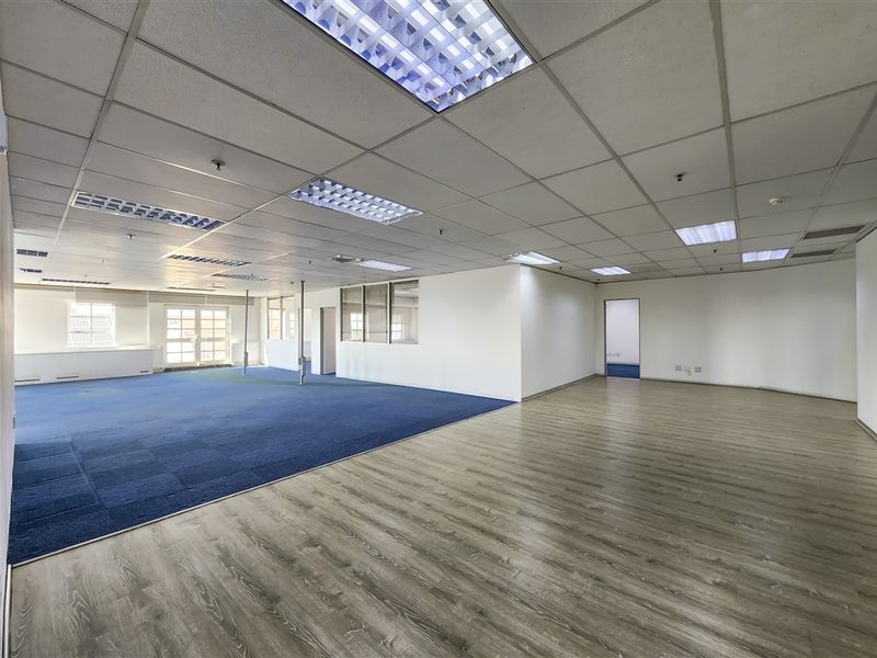 Spacious open-plan office area featuring a mix of carpet and laminate flooring, suspended ceilings with recessed lighting, and internal glass partitioning.