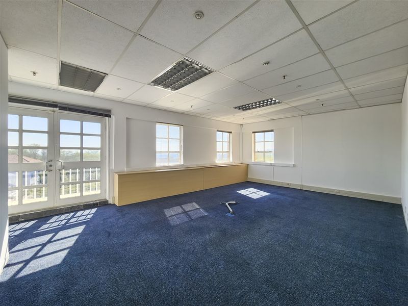 Spacious empty office area featuring a suspended ceiling, recessed lighting, built-in cabinetry, and access to an outdoor balcony through double glass doors.