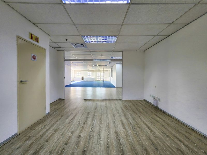 A vacant office space featuring laminate flooring, a suspended ceiling with recessed lighting, and a glass partition leading to an adjacent area.