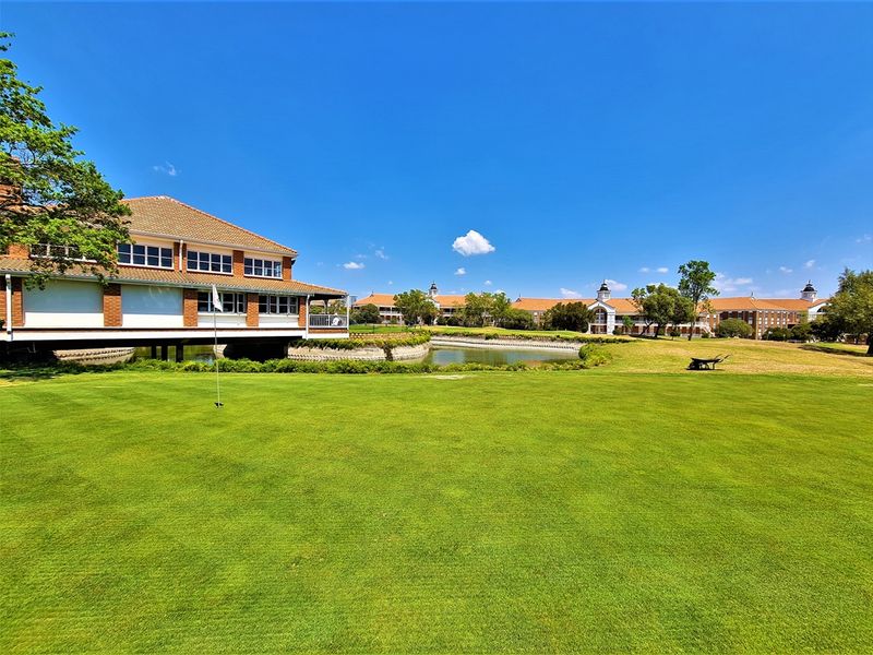 A scenic view of the office complex exterior featuring a manicured lawn, putting green, and a tranquil pond set against the building facade.