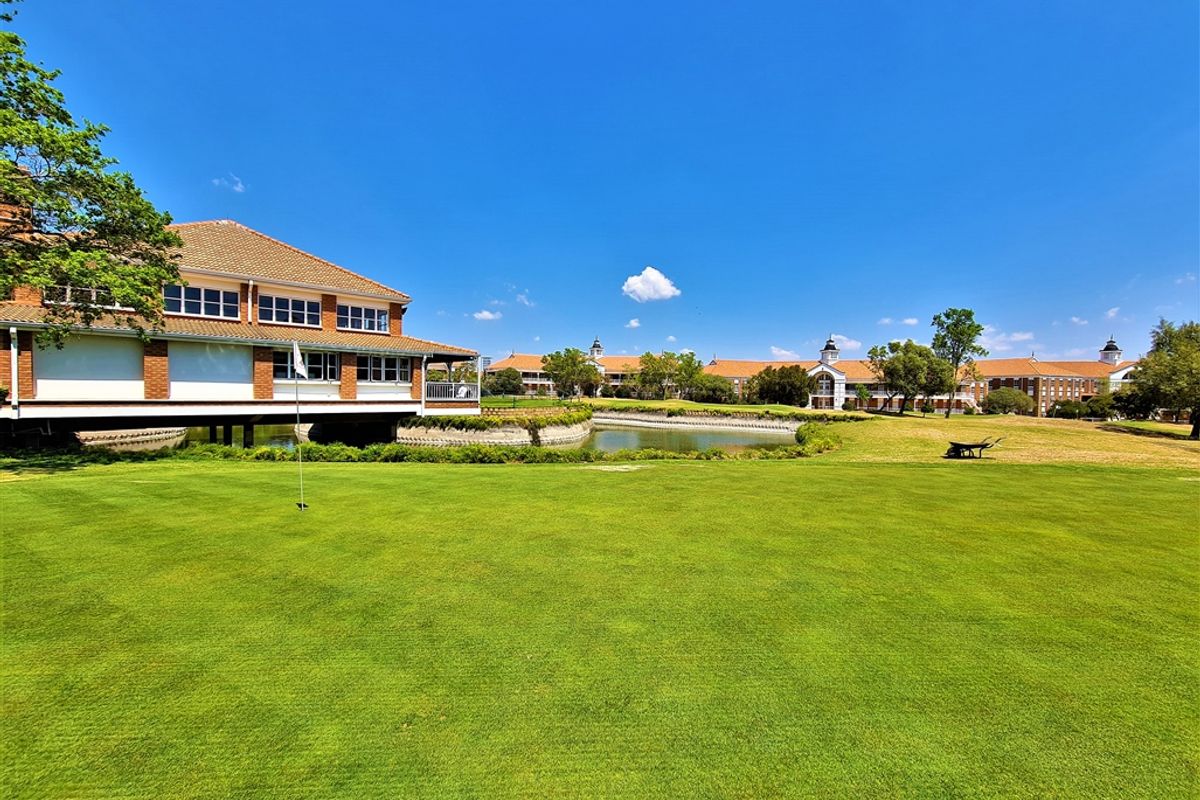 A scenic view of the office complex exterior featuring a manicured lawn, putting green, and a tranquil pond set against the building facade.