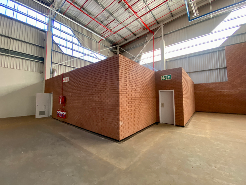 Spacious industrial utility area featuring exposed steel roof trusses, fire suppression systems, and solid brick partition walls with concrete flooring.