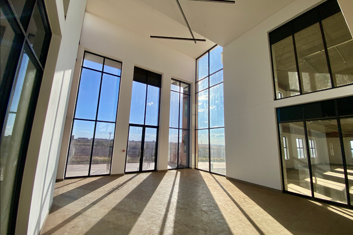 Spacious, double-volume industrial living area featuring expansive floor-to-ceiling windows, tiled flooring, and modern architectural lighting, offering abundant natural light and open views.