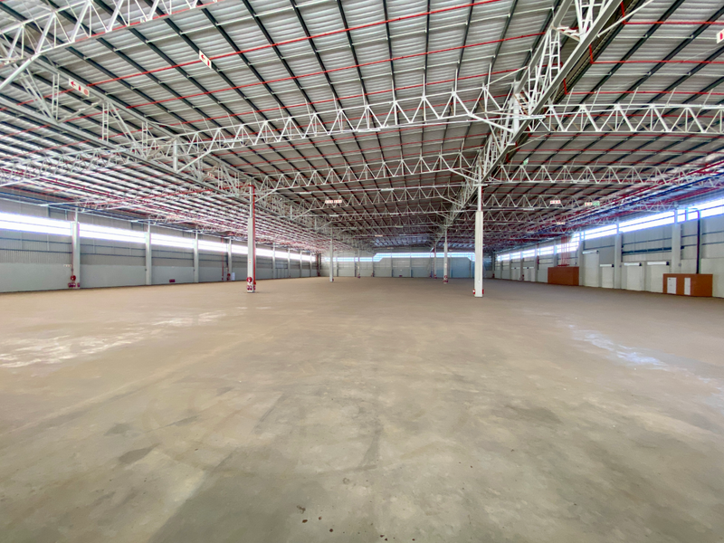A large, open-plan industrial warehouse space featuring high ceilings with exposed steel trusses, fire sprinkler systems, and polished concrete flooring.