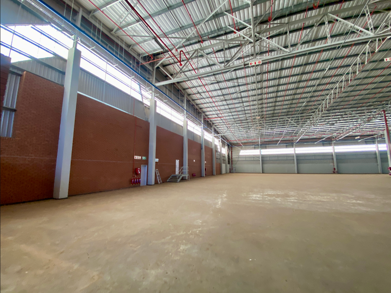 Spacious industrial warehouse featuring high ceilings with exposed steel trusses, fire sprinkler system, concrete flooring, and large brick walls with clerestory windows.