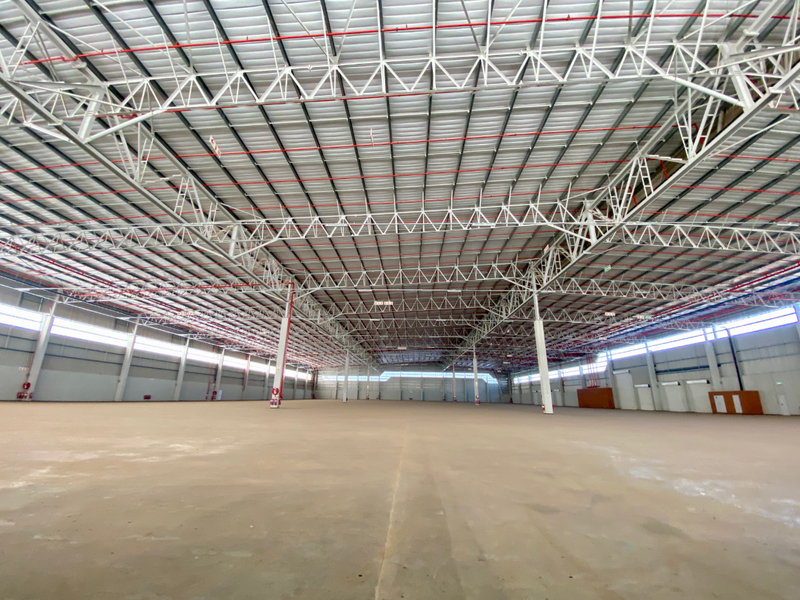 Expansive industrial warehouse space featuring high ceilings with exposed steel trusses, fire sprinkler systems, and polished concrete flooring.